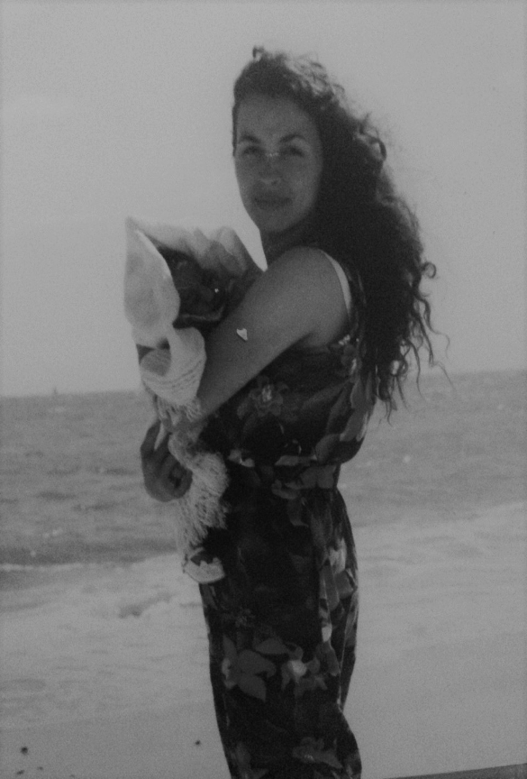 A young woman standing carrying a baby on a beach